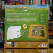 Trasera del juego 'My City' disponible en Mana House – Campaña de 24 partidas, Modificación permanente del tablero, Modo alternativo post-campaña, Reglas progresivas, Desarrollo urbano por eras.